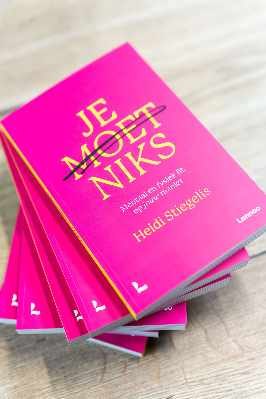 Een stapel exemplaren van het boek ‘Je moet niks’ van Heidi Stiegelis, roze met gele letters